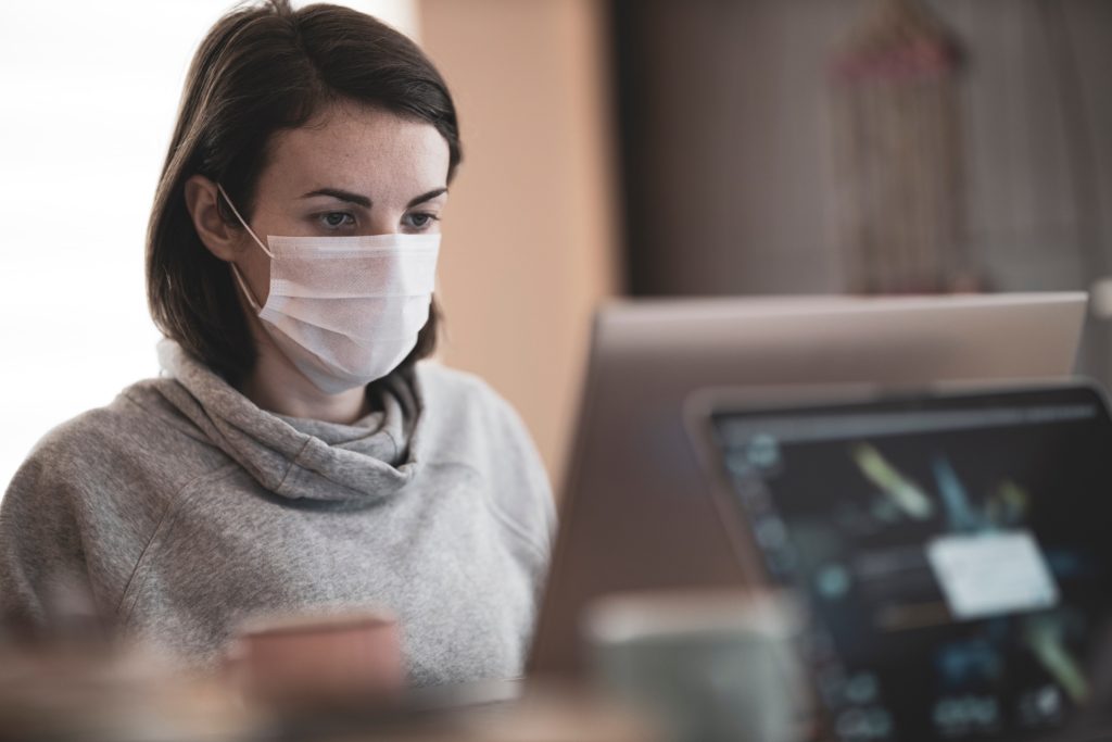 A woman wearing a face mask while working on her computer.
