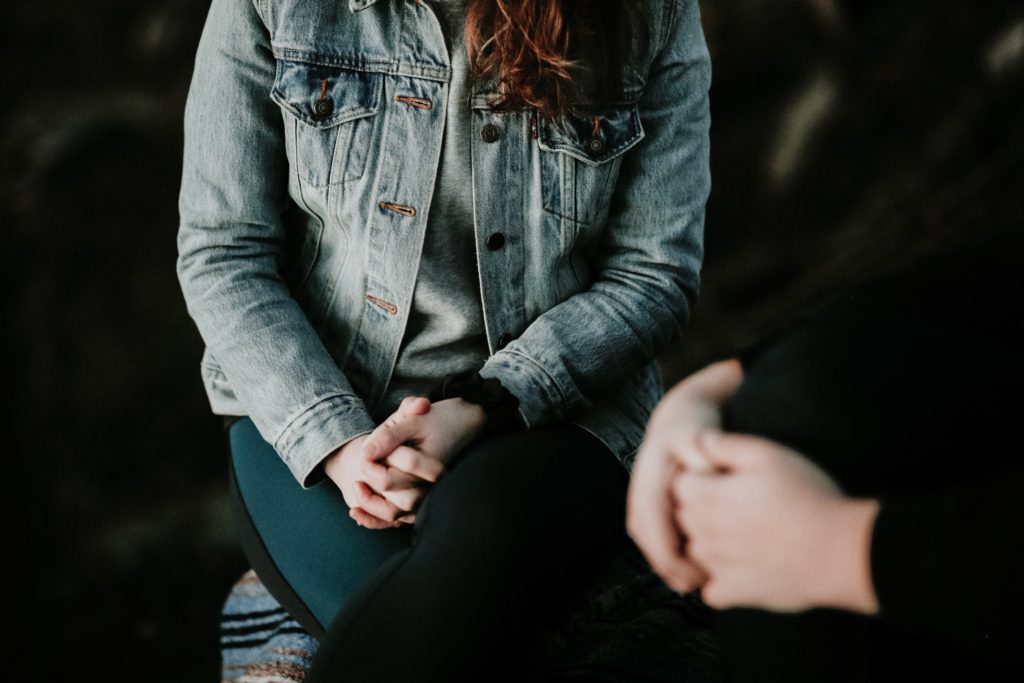 A person wearing a denim jacket sitting across another person with hands clasped
