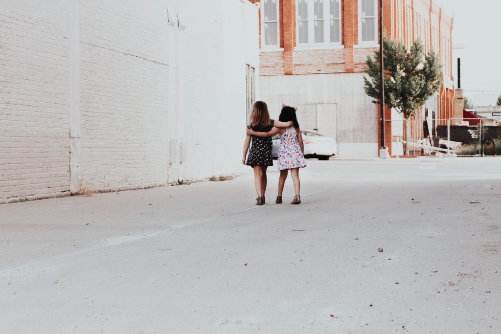 Two girls walking down a street with their arms around each other