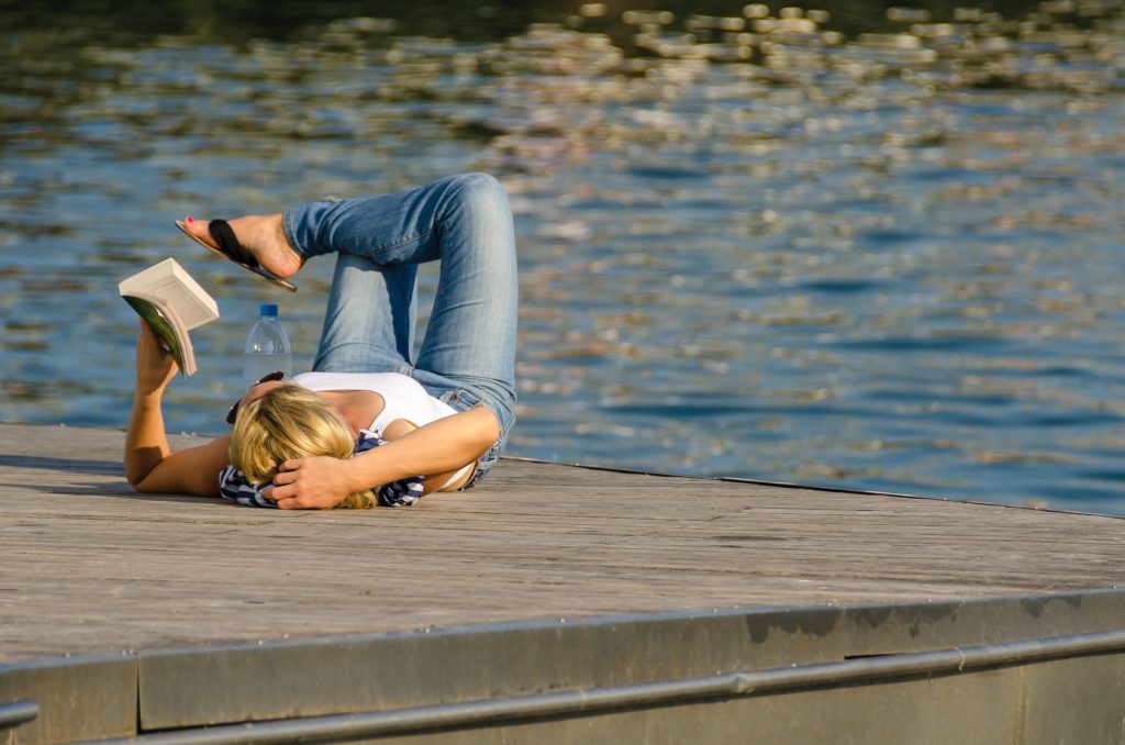 A person reading a book while lying down by the water