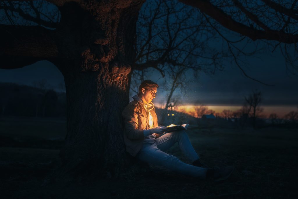 夜の木の下で本を読んでいる男性