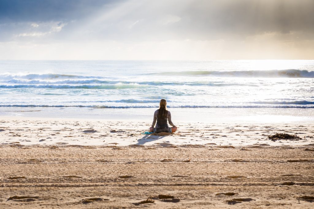 A woman sitting on the beach in meditation