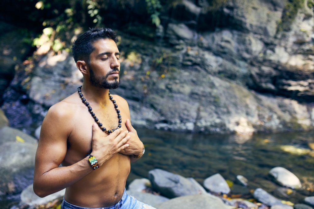 A man sitting by a river with his hands to his chest