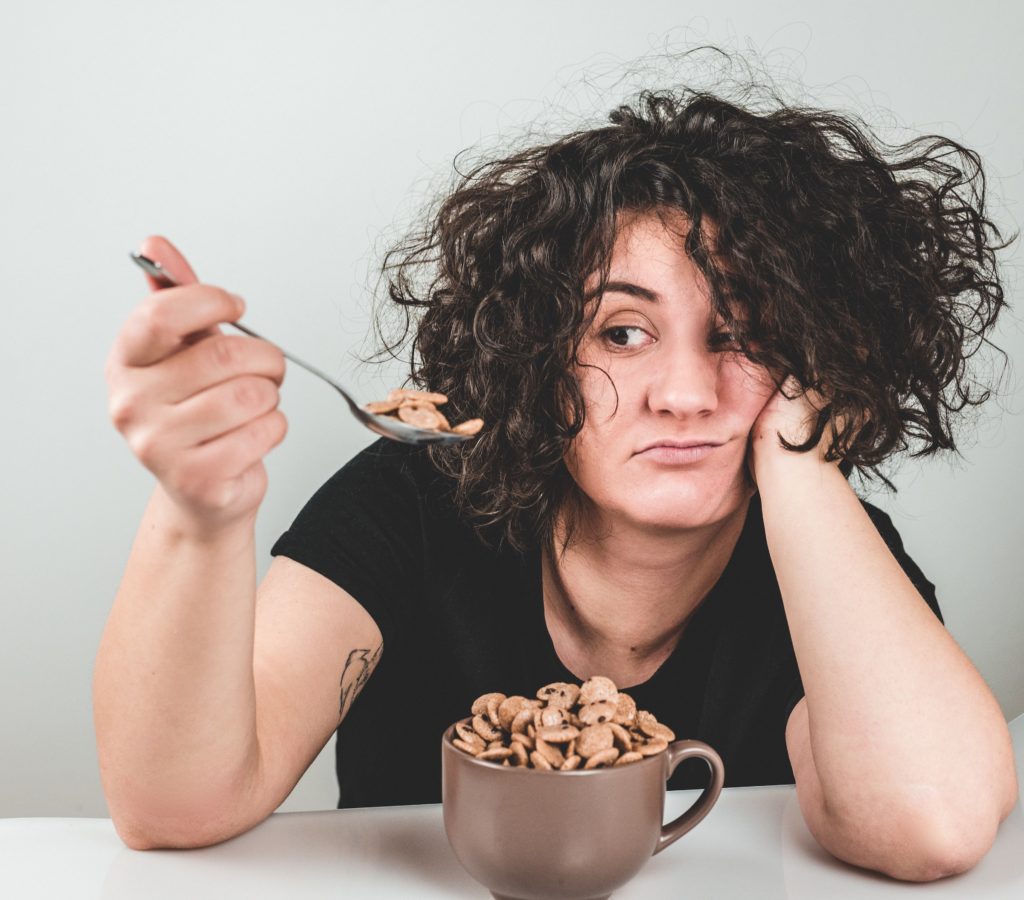 A woman looking at a spoon full of cereal 