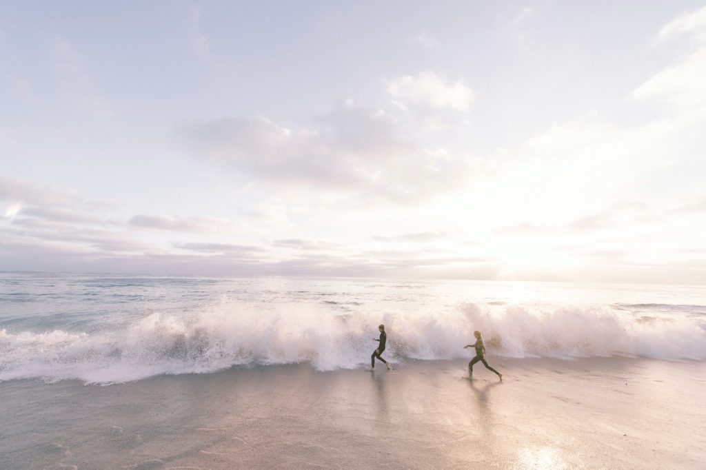Two people running towards the wave on a beach