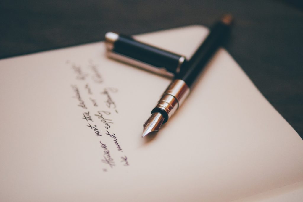 A black and silver fountain pen resting on paper with handwritten words