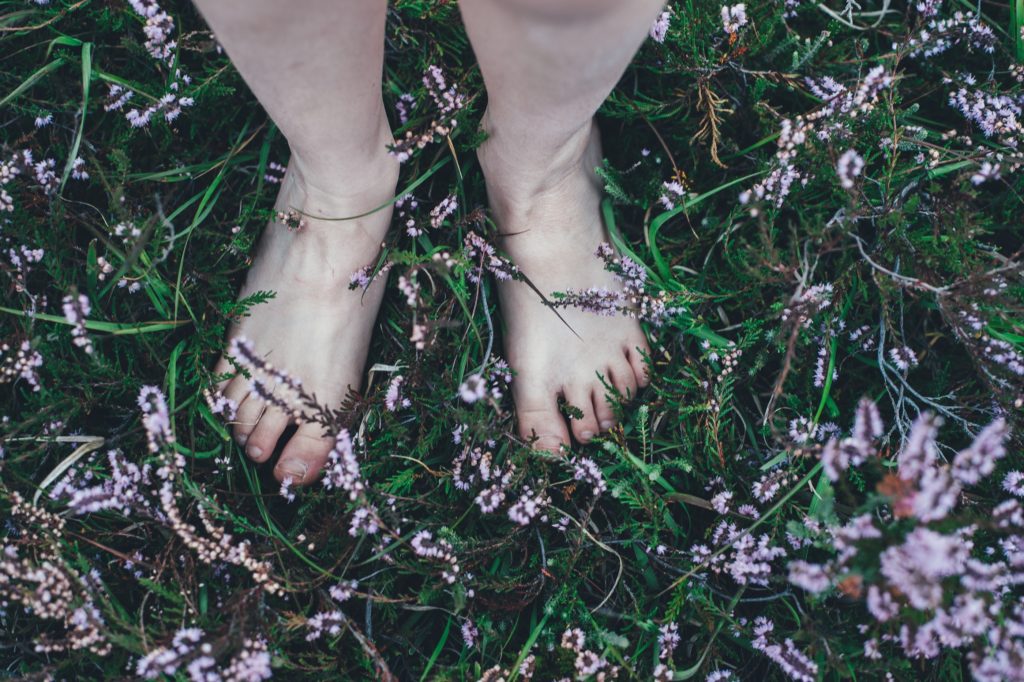 A person standing bare feet on a field of wild flowers.