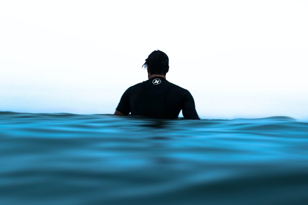 A man half submerged in the ocean looking out to the horizon.