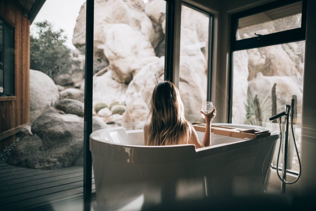A woman soaking in the tub while holding a drink and looking outside.