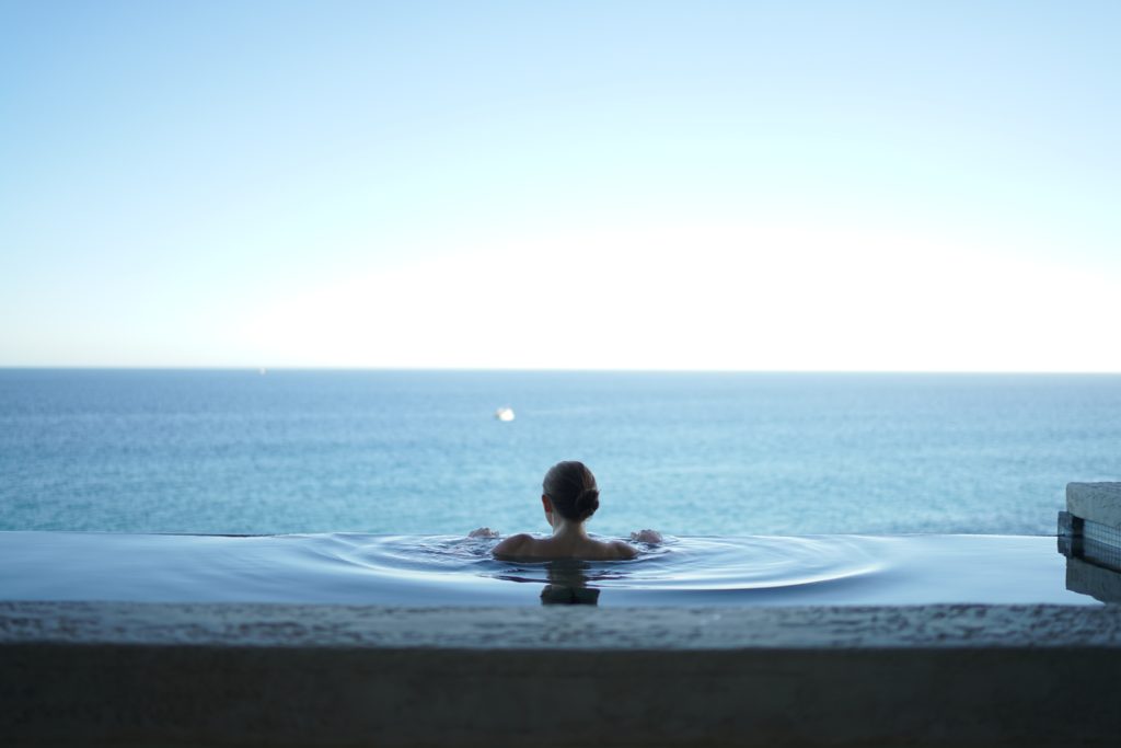 A woman soaking in an infinity pool outlooking the ocean.