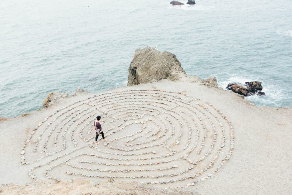 A man taking a meditational walk through a labyrinth of rocks. 