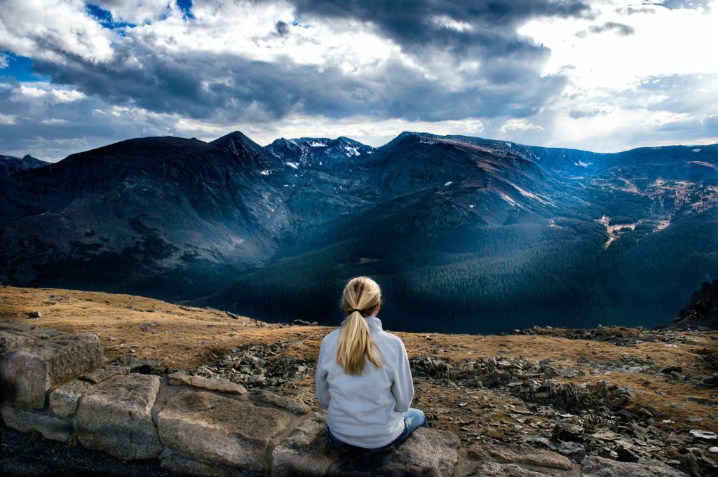 A woman sitting on a mountainside looking out at the scenery
